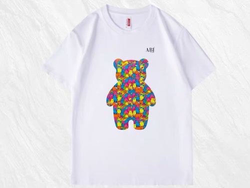 *Alaska Collection
A white short-sleeve T-shirt featuring a colorful teddy bear with salmon fish graphic made of small geometric shapes on the front. 